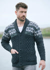 Man wearing a patterned cardigan standing outdoors with a body of water in the background