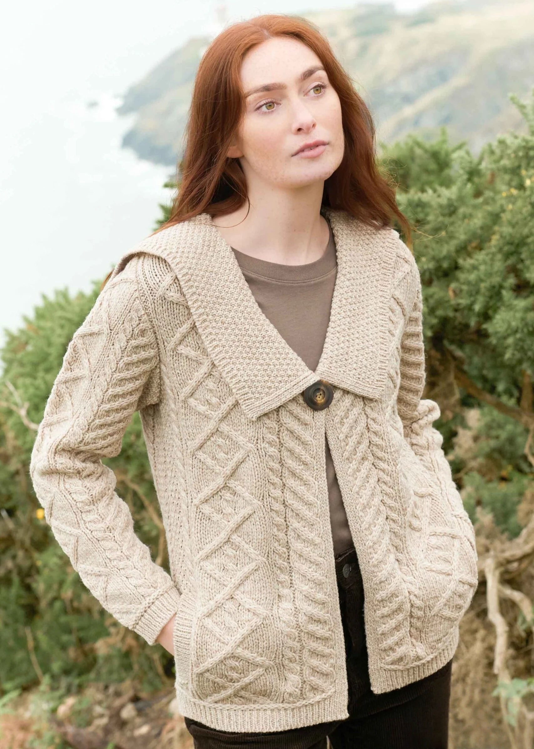 Woman wearing a beige knitted cardigan outdoors with trees in the background