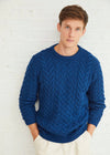 Man wearing a blue cable knit aran sweater against a white brick wall