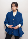 Woman wearing a blue aran knitted cardigan with a plain background