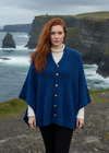 Woman wearing a blue aran knitted cardigan with a plain background