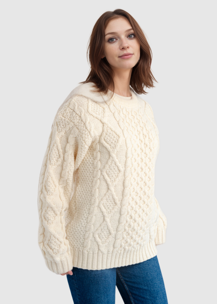 Woman wearing a cream cable knit sweater and blue jeans on a white background