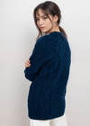Woman wearing a dark blue cable knit sweater against a white background
