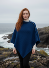 Woman wearing a blue aran poncho on a white background