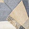 Close-up of a checkered blanket with beige and gray colors and fringed edge.