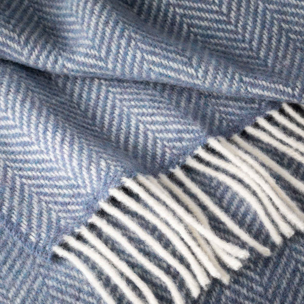 Close-up of a blue herringbone patterned fabric with white fringe.