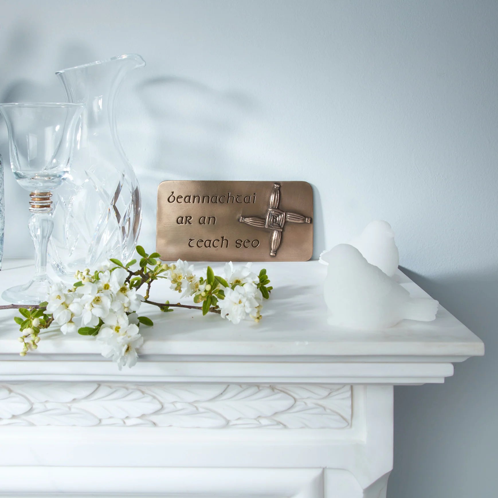 Decorative plaque with a cross on a white surface with flowers and a vase.