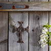Decorative metal cross on a wooden surface with white flowers and green leaves.
