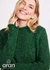 Woman wearing a green knitted sweater with 'aran' branding on a white background