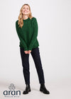 Woman wearing a green sweater with 'Aran Woollen Mills' branding on a white background
