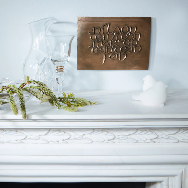Decorative wooden plaque with engraved text on a white surface with glass pitcher and candle.