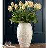 White textured vase with pink roses on a wooden surface against a dark background