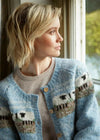 Woman wearing a blue knitted cardigan with sheep pattern, sitting by a window.