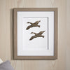Framed artwork of two flying ducks on a wooden wall.