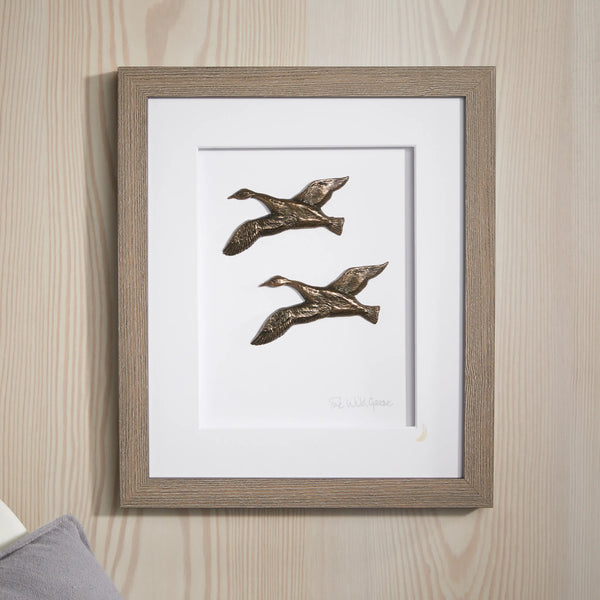 Framed artwork of two flying ducks on a wooden wall.