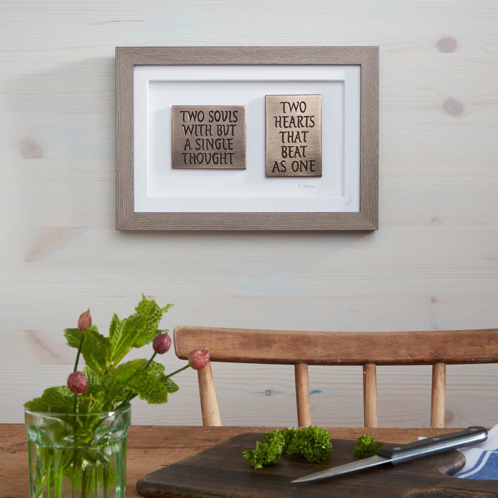 Framed wooden signs with romantic quotes on a wall above a wooden table.