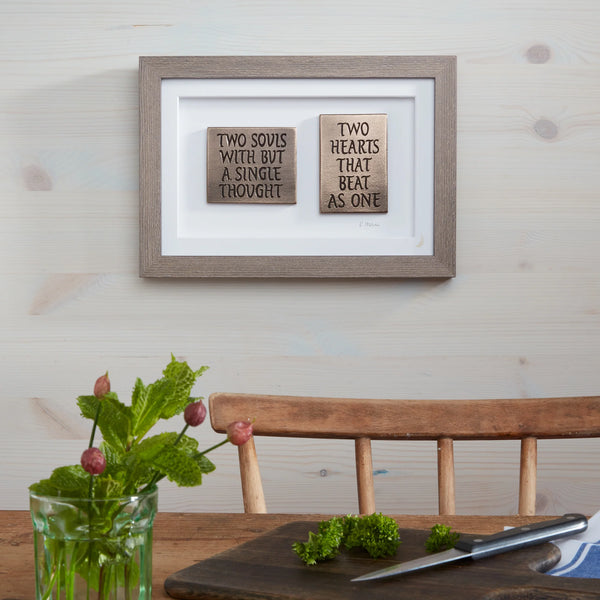 Framed wooden signs with romantic quotes on a wall above a wooden table.
