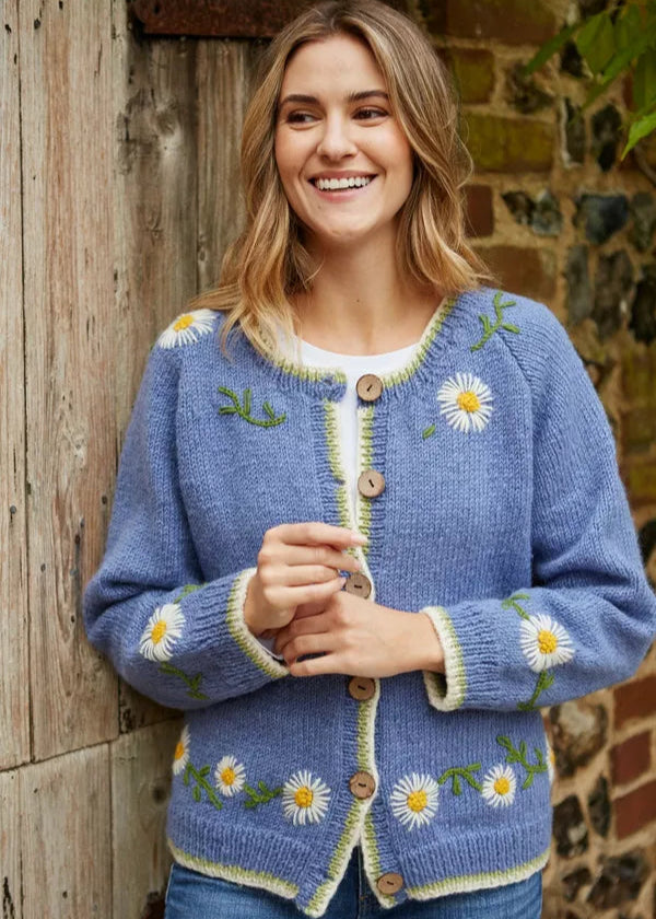 Woman wearing a blue cardigan with floral patterns against a rustic stone wall.