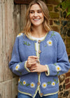 Woman wearing a blue cardigan with floral patterns against a rustic stone wall.