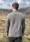 Man wearing a gray sweater standing in a mountainous landscape