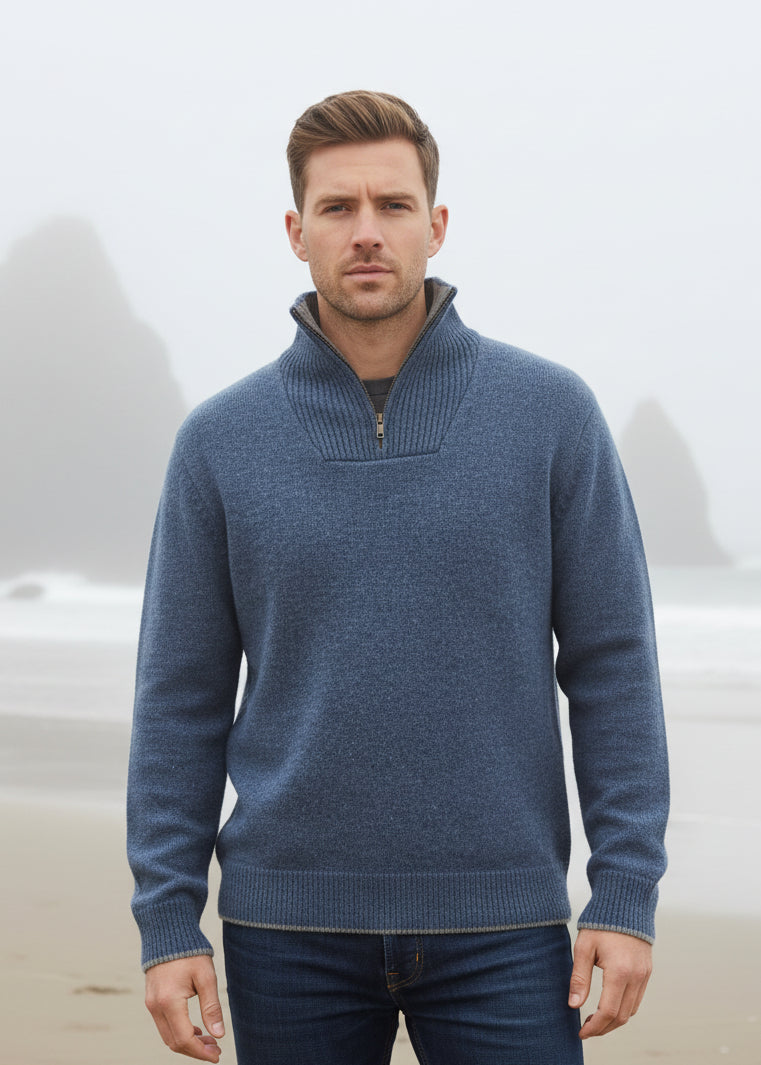 Man wearing a blue sweater sitting on a cliff overlooking the ocean.