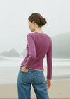 Woman wearing a purple sweater and blue jeans standing on a beach.