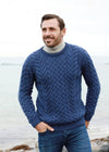Man wearing a blue aran knitted sweater standing on a rocky shoreline.
