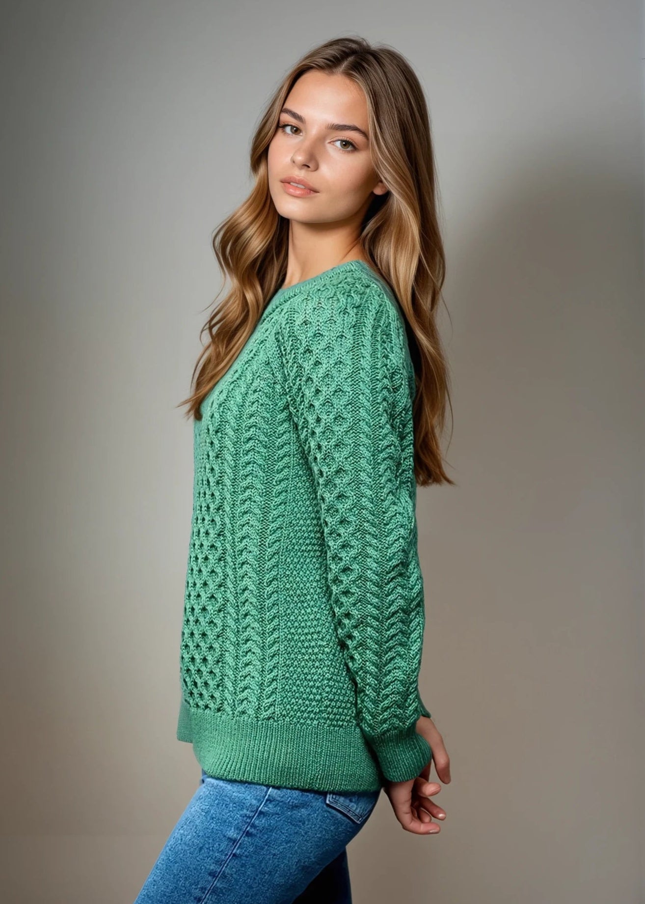 Woman wearing a green knitted aran sweater against a plain background