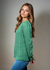 Woman wearing a green knitted aran sweater against a plain background