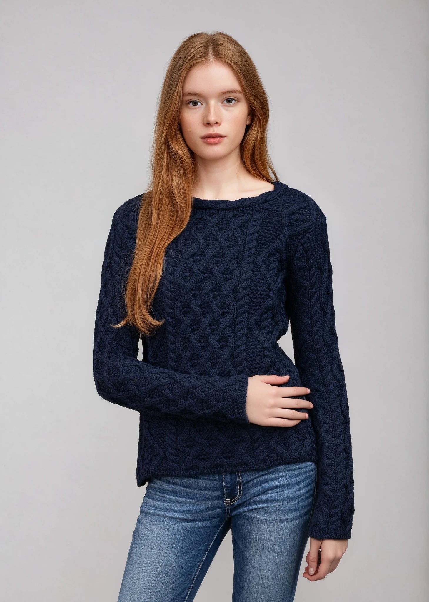 Woman wearing a dark blue cable knit sweater and jeans on a gray background