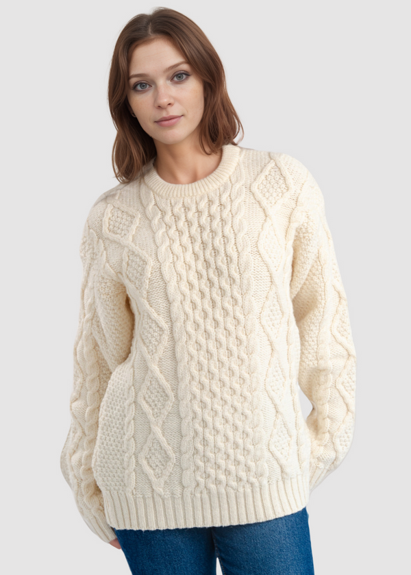 Woman wearing a cream aran cable knit sweater on a light gray background