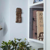 Decorative wall piece on a light blue wall next to a white shelf with books and a plant.