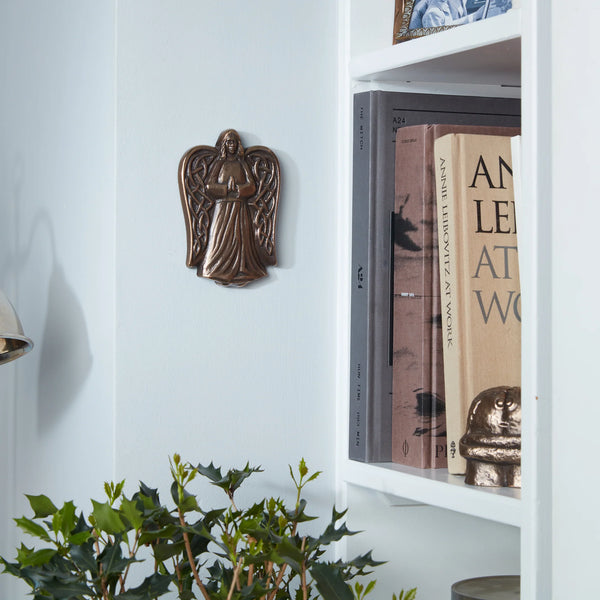Decorative angel wall plaque on a white shelf with books and a plant.