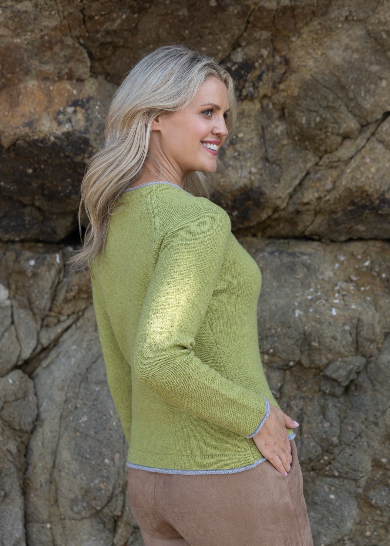 Woman wearing a green sweater standing against a rocky background