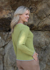 Woman wearing a green sweater standing against a rocky background