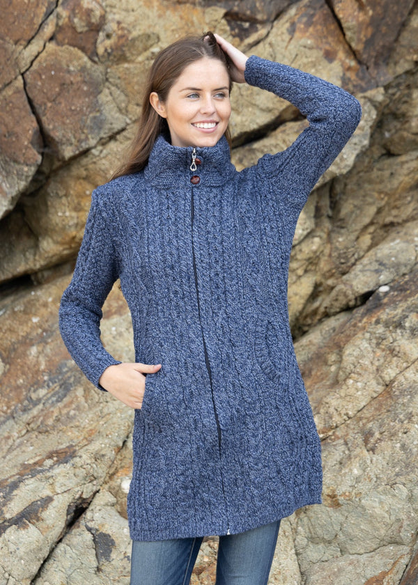 Woman wearing a blue knitted coat standing against a rocky background