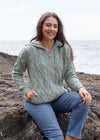 Woman wearing a green knitted hoodie sitting on rocks by the water