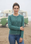 Woman wearing a green sweater on a beach with ocean and rocks in the background