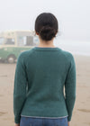 Woman wearing a green sweater standing on a beach looking out at the ocean.
