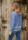 Woman wearing a blue knitted sweater with floral patterns in front of a wooden door.
