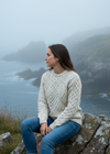 Woman in a white sweater sitting on a rock with a foggy mountain landscape in the background