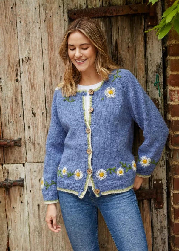 Woman wearing a blue knitted cardigan with floral patterns standing in front of a wooden door.