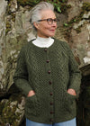 Woman wearing a green aran knitted cardigan in front of a stone wall.