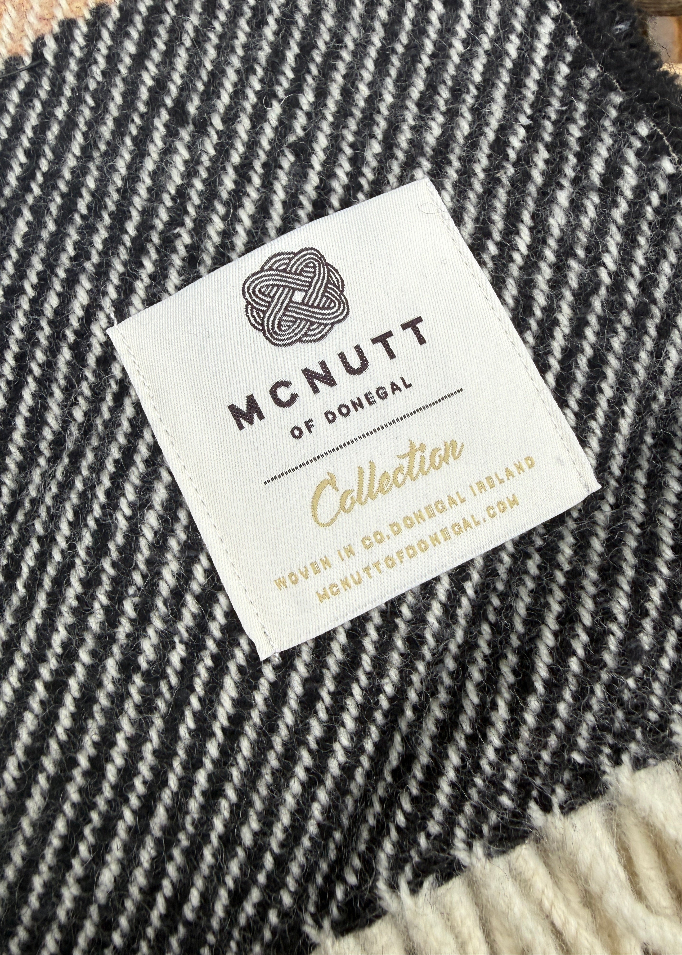 Close-up of a black and white textured woven blanket with a white brand label reading 'MCNUTT OF DONEGAL Collection'.