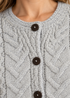 Close-up of a light gray cable-knit cardigan sweater with three dark brown buttons, worn by a model.