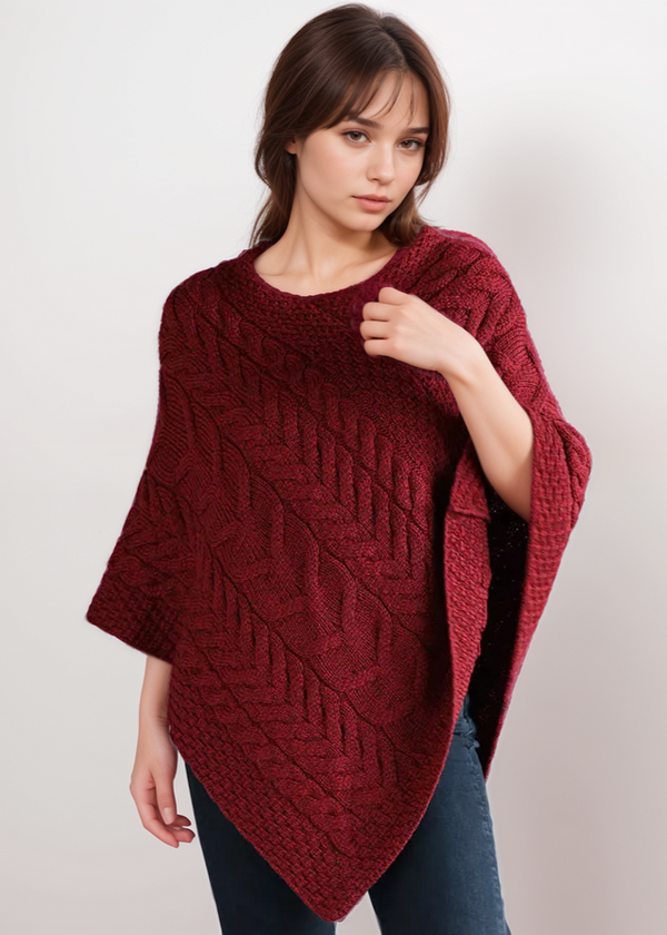 Woman wearing a red knitted aran poncho against a plain background