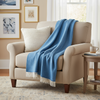 Beige armchair with a blue blanket and white pillow in a cozy living room setting.