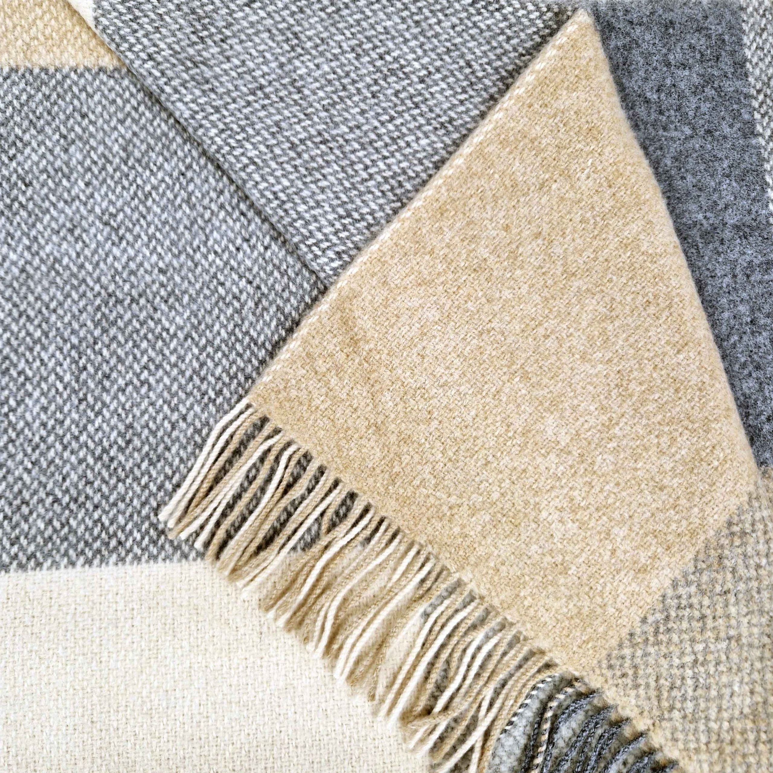 Close-up of a checkered blanket with beige and gray colors and fringed edge.