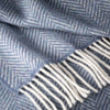 Close-up of a blue herringbone patterned fabric with white fringe.