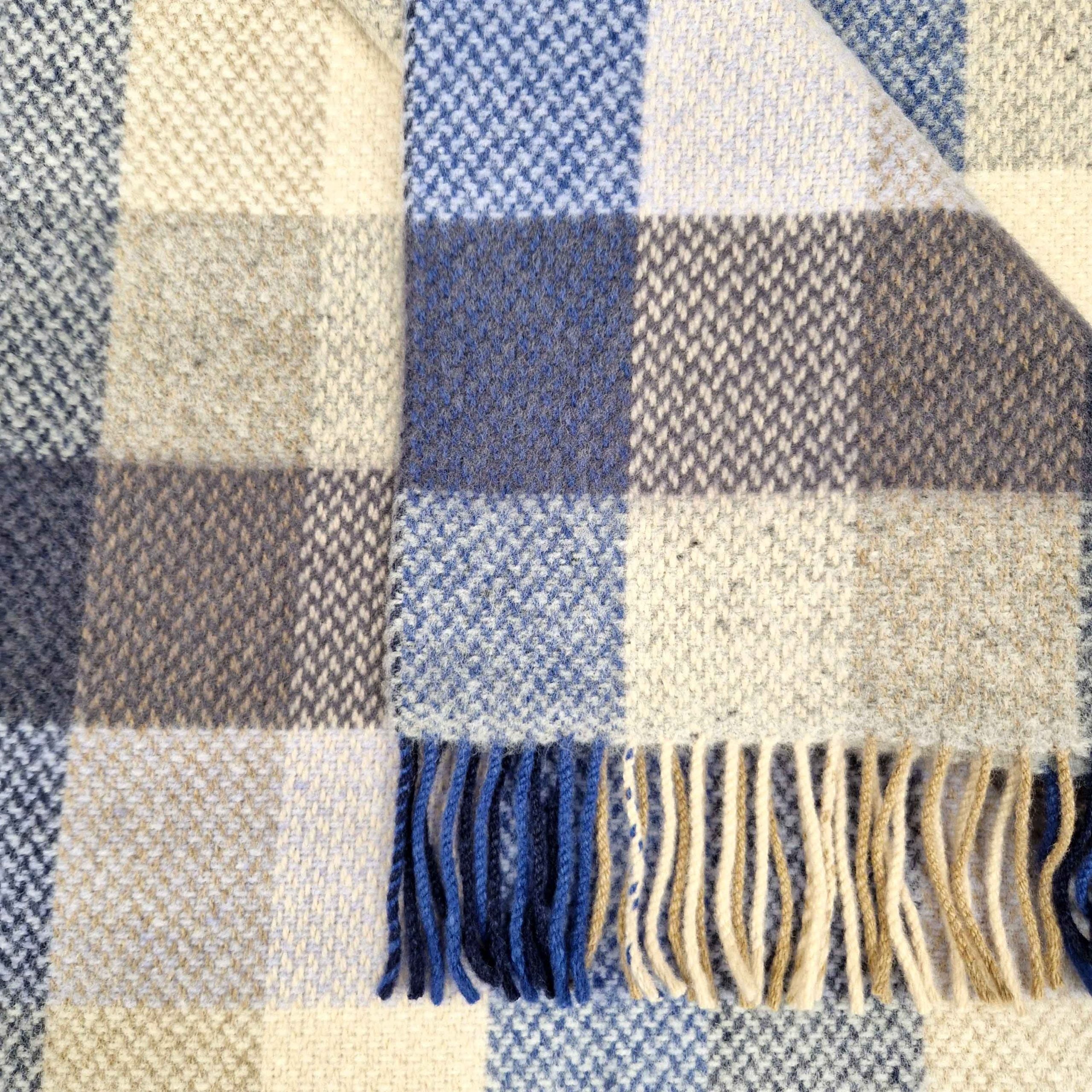 Close-up of a checkered fabric with blue, beige, and gray colors and fringed edges.